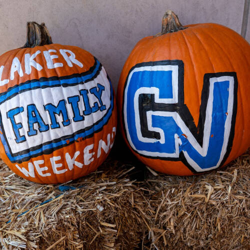 two painted pumpkins on a hay bale; left reads Laker Family Weekend, right is GV in white, blue and black